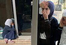 Girls wearing headscarves look out from school window, appearing worried and anxious.