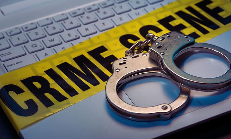 Handcuffs placed on a keyboard with crime scene tape in the background.