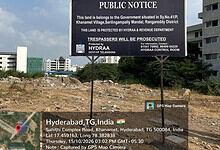 Public notice on land protection in Hyderabad, India, with city buildings in the background.
