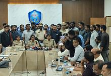 Police officials and officers at a press conference in a conference room with media personnel present.