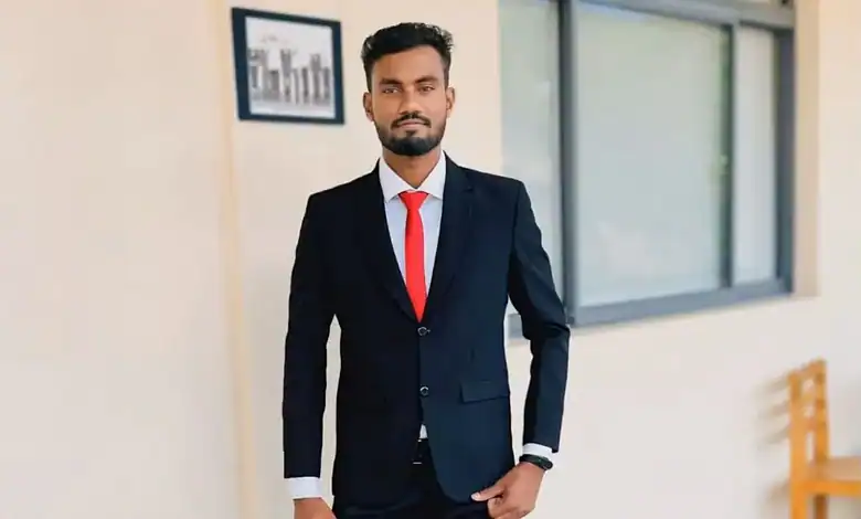 Man in a dark suit with red tie standing in office corridor.