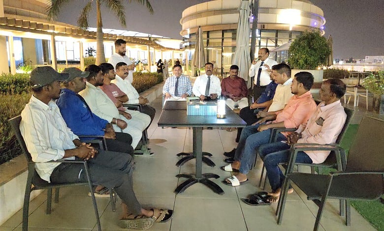 Group of Telugu workers and Oman company representatives in discussion on rooftop terrace.